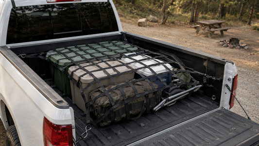 Black Tesheer truck bed cargo net secured over storage bins, a duffel, cooler, and folded camping chair in a pickup bed