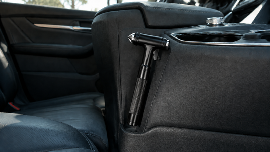 Black Tesheer car window breaker and seatbelt cutter stored beside a center console
